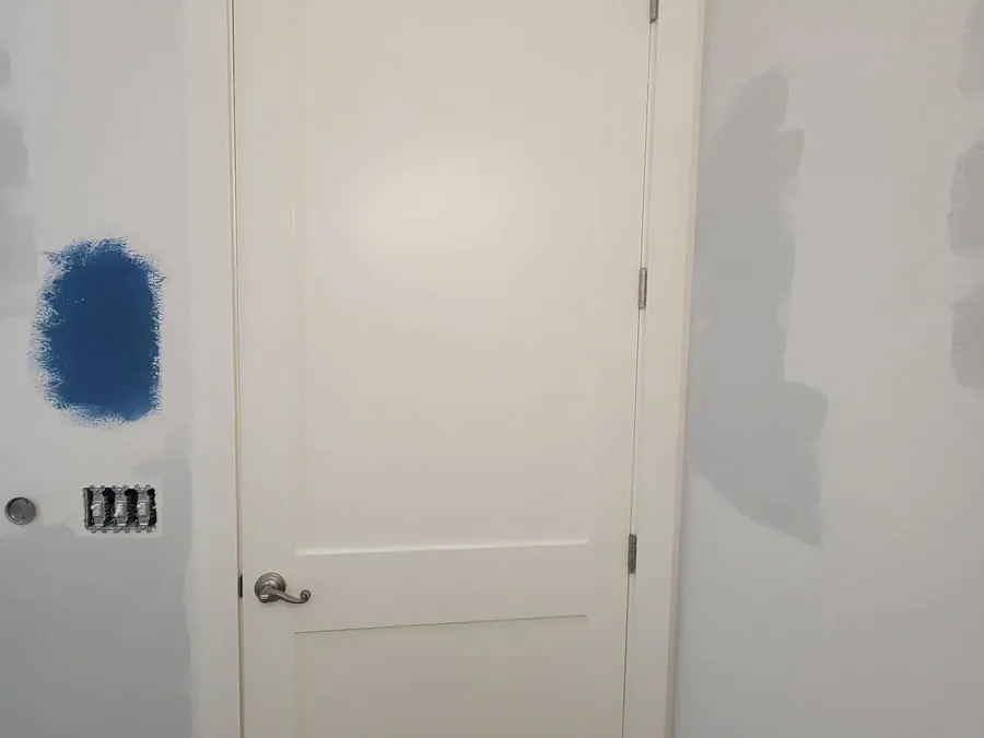 Plain white paneled bathroom door before painting, with a blue paint sample swatch on the wall beside it