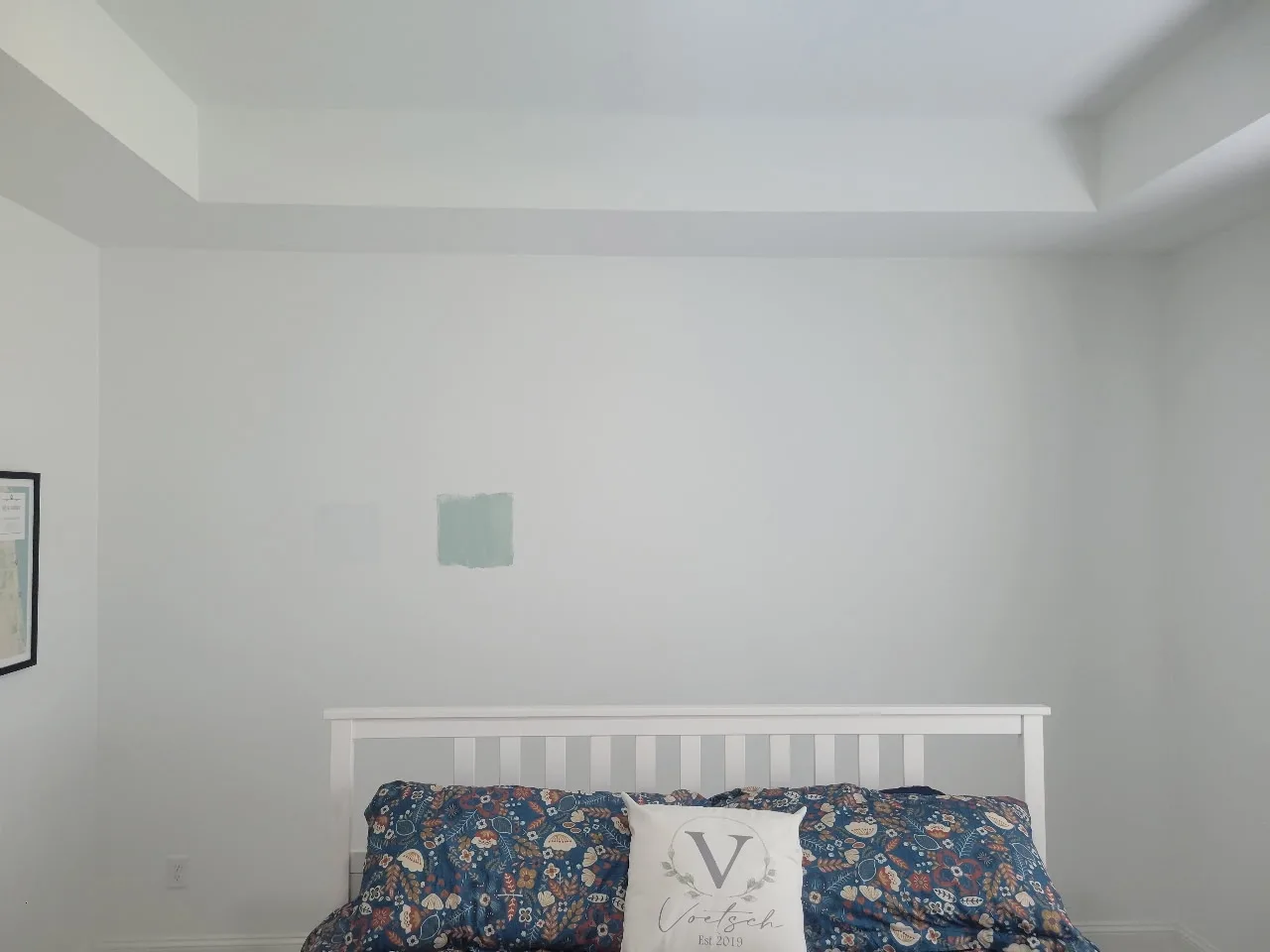 Plain white bedroom wall with two paint color swatches before painting