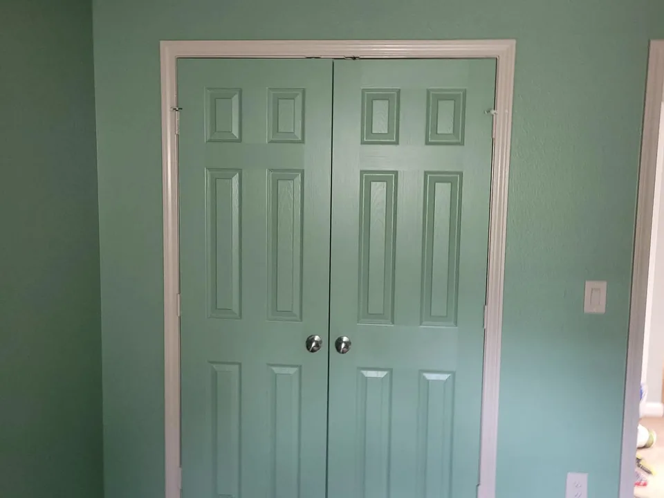 The same bedroom walls and closet doors finished in a soft sage green with crisp white trim