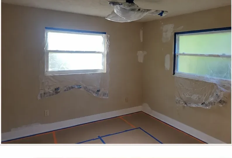 Dated tan bedroom with taped windows and floor before painting