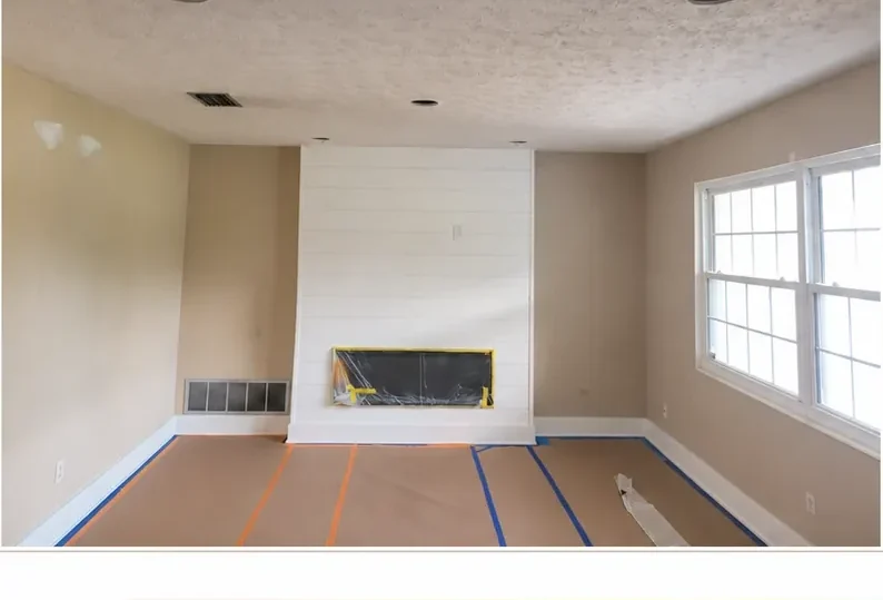 Beige living room mid-prep with a masked fireplace and taped floor before painting