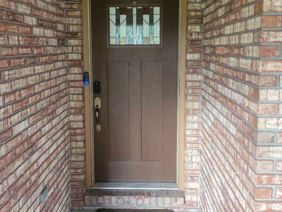 Worn brown front door with dated tan-mortar brick surround before painting