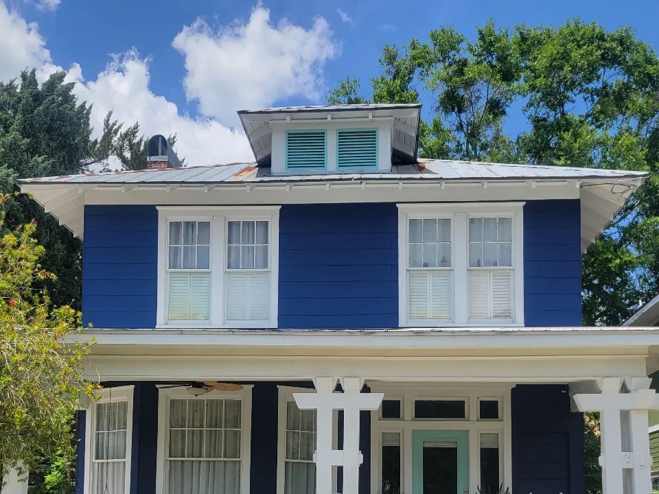 The same historic home finished in rich navy blue with white trim, a mint-green front door and porch columns