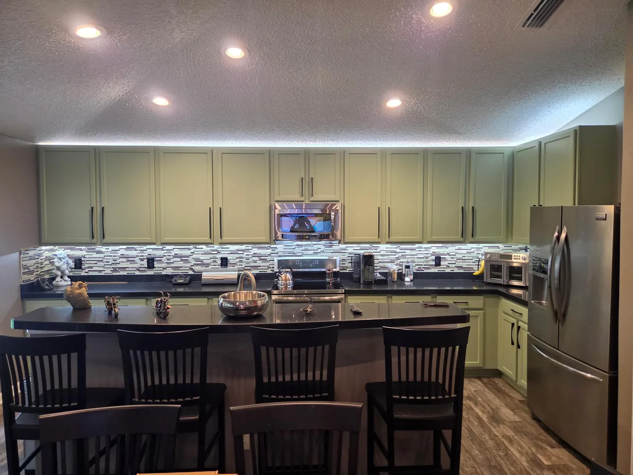 The same kitchen cabinets refinished in a soft sage green with dark hardware and the original counters and backsplash