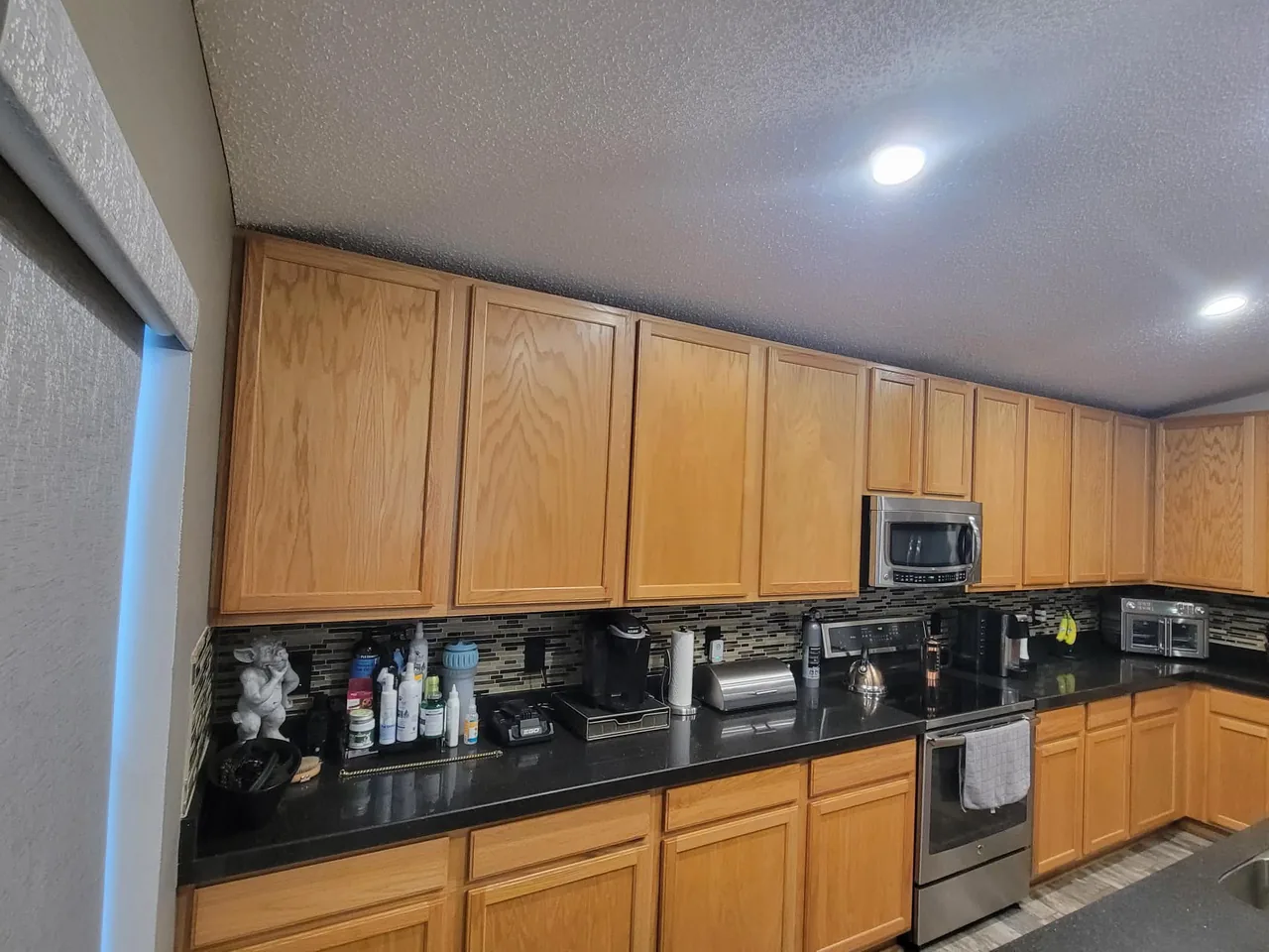 Dated honey-oak kitchen cabinets with a dark counter and tile backsplash before refinishing