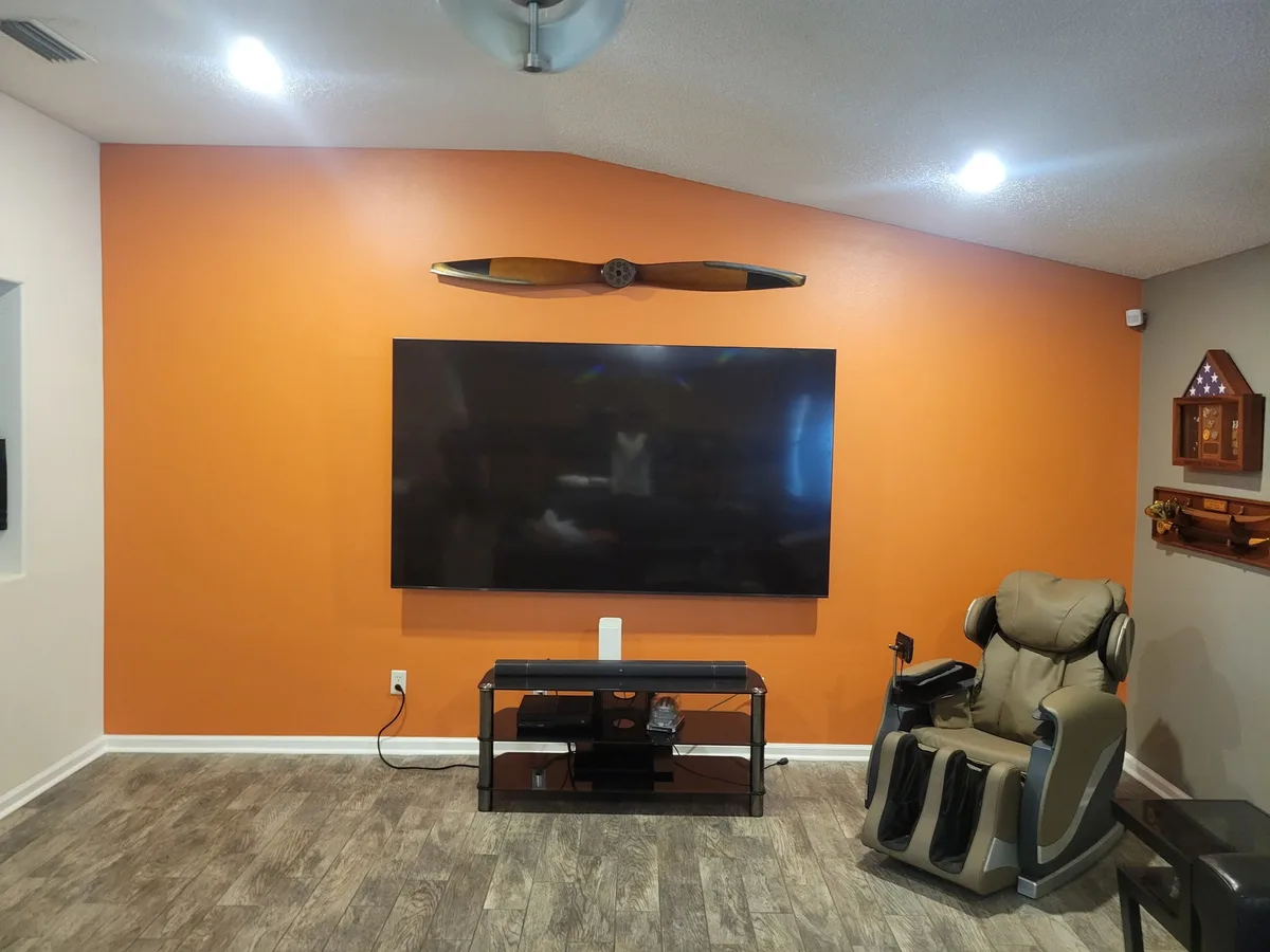 The same media room wall finished in bold burnt-orange with a vintage wooden airplane propeller mounted above the TV
