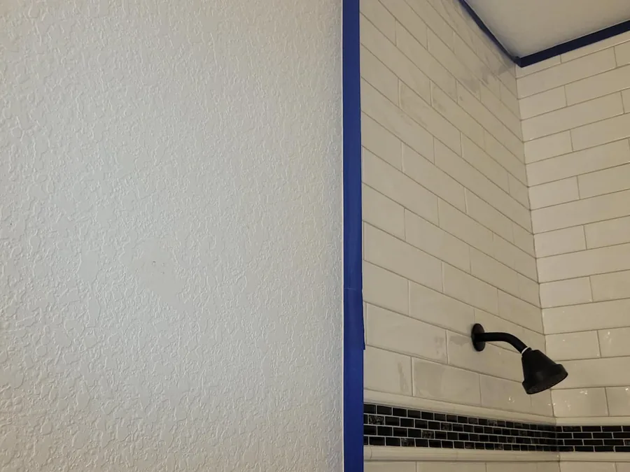 White subway-tile shower corner masked with painter's tape, walls not yet painted
